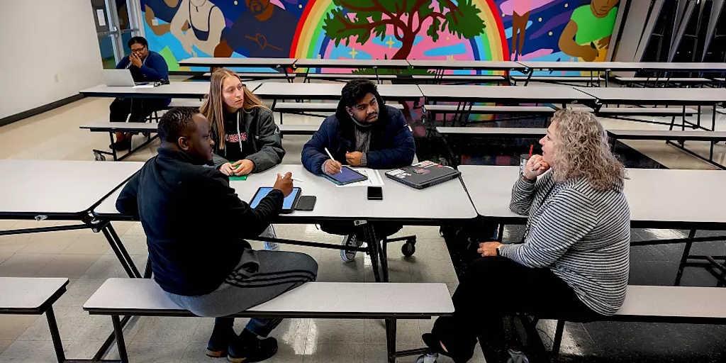 Three students and a client sitting at long cafeteria table at Hawthorne Food Pantry