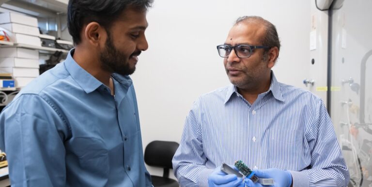 BMEI faculty and INDI lab director Mangilal Agarwal in lab with research assistant, holding a device (photo by Liz Kaye, Indiana University)